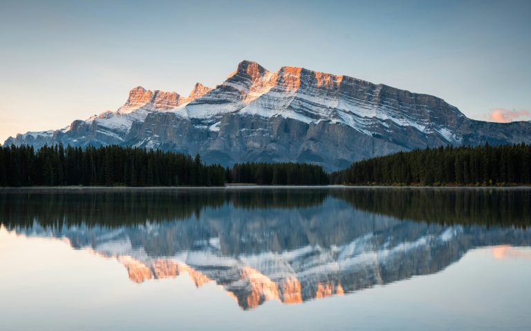 Snowy mountain peaks reflected in a calm lake surrounded by pine trees