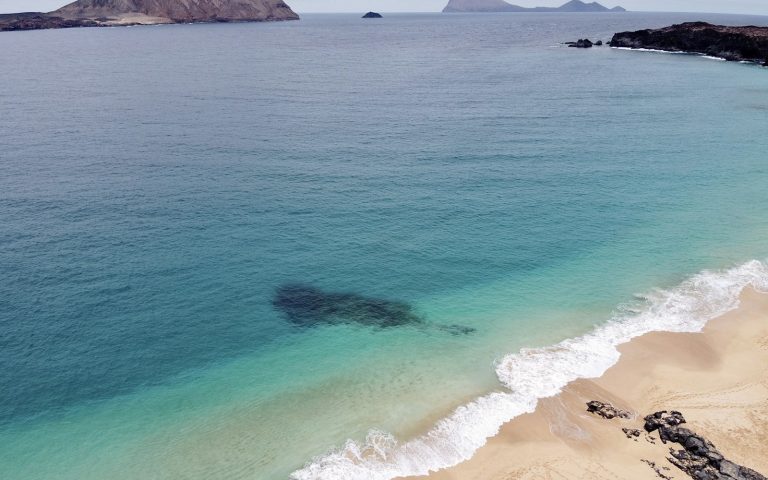 Waves breaking on a sandy beach beneath volcanic cliffs