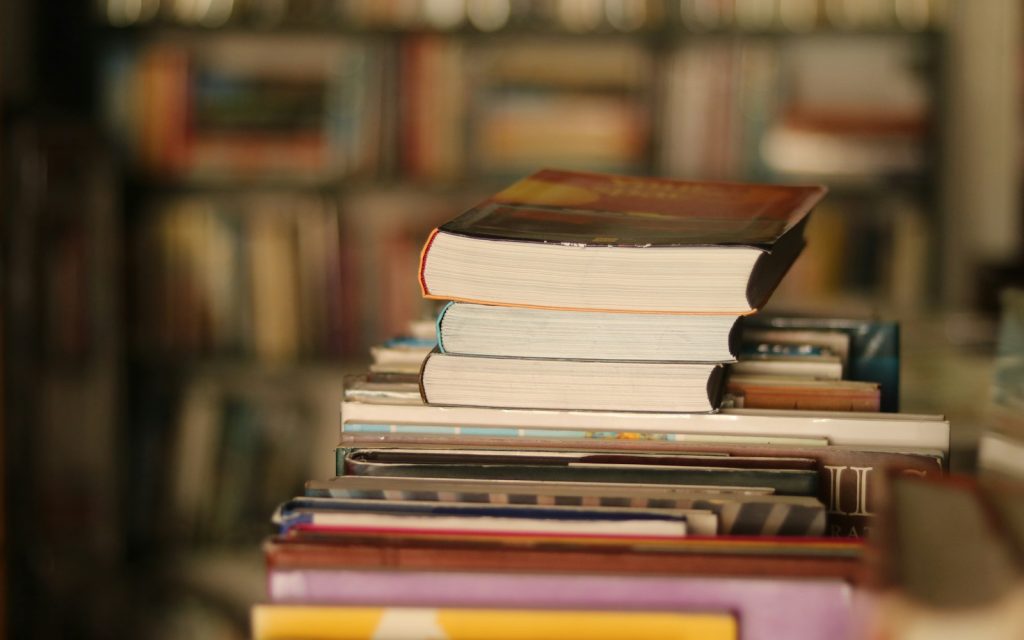 A stack of novels in front of a full bookshelf