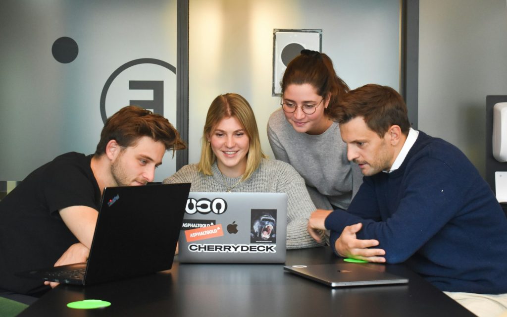 Four colleagues collaborating around a laptop in a modern office