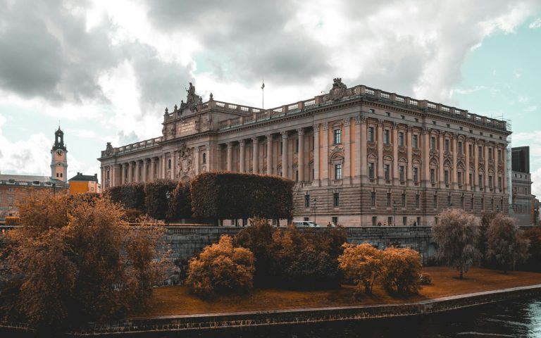 Grand classical building beside a river framed by autumn trees